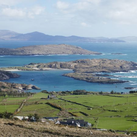 Panoramic landscape of County Kerry, showing the contrast between the green countryside and the blue waters of the Atlantic Ocean, with islands in the distance