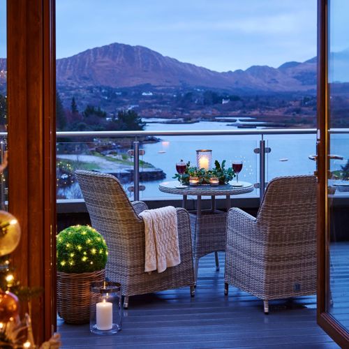 A hotel balcony in Sneem, Ireland, is decorated for Christmas with a lit tree visible inside and a stunning view of a lake and mountains outside